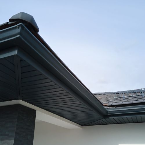 House corner with brown metal planks siding and roof with steel gutter rain system. Roofing, construction, drainage pipes installation.
